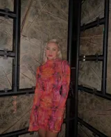 Vestido corto de microtul elastizado con estampado floral en tonos naranja, rosa y negro. Tiene cuello alto y mangas largas acampanadas.