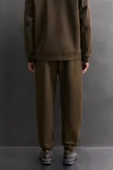 Pantalón jogger de entrenamiento, corte regular fit, color verde oliva oscuro. Confeccionado en tejido técnico compacto de algodón con elasticidad y efecto neopreno. Presenta cintura elástica ajustable con cordón blanco, bolsillos frontales y un bolsillo lateral con cierre de cremallera. El bajo termina en puño.