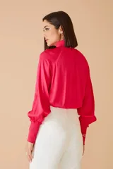 Blusa fucsia de satén con cuello alto fruncido y mangas largas abullonadas con puños elásticos.