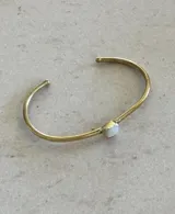 Pulsera rígida dorada con una piedra redonda de nácar en el centro.