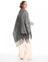 Ruana de tejido tweed en tonos verdes con destellos de lurex, diseño abierto con terminación de flecos en los bordes.