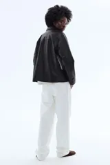 Campera negra de cuero sintético con solapas de muesca, cierre frontal de botones oscuros y bolsillos laterales ribeteados. Presenta costuras de canesú en el frente y en la espalda, y diseño forrado.