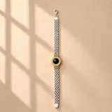 Pulsera de plata y oro de 18k con eslabones entrelazados y un dije central circular con detalles dorados y una piedra de ónix negro.