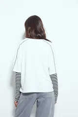 Remera de manga corta con silueta relajada y costuras a la vista en color blanco que contrastan sobre el tejido negro. Presenta un diseño moderno con terminaciones destacadas.