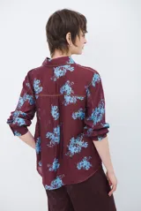 Camisa de corte clásico con cuello camisero y cierre frontal de botones, confeccionada en tela color bordó con estampado floral en tonos celestes.