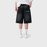 Bermuda baggy de denim negro con efecto acid wash, corte holgado y bolsillos traseros con detalle de bordado cursivo en blanco.