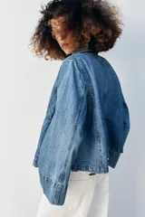 Campera de denim azul con cuello solapa, cierre frontal de botones metálicos, bolsillos delanteros de plastrón y mangas largas acampanadas.