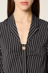 Camisa corta de popelina a rayas con mangas abullonadas, cuello solapa y cierre frontal con botón decorativo. Presenta un diseño con efecto plisado en el pecho y corte ajustado.