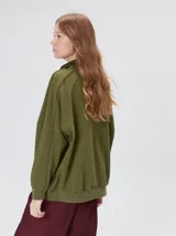 Buzo verde militar de algodón suave, de calce oversize, con cuello alto y cierre frontal parcial metalizado. Cuenta con bolsillos laterales con cierre y puños y ruedo elastizados.