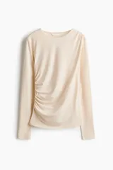 Top de punto de crepé color beige, de ajuste ceñido, con mangas largas y escote redondo. Presenta un diseño con frunces en un hombro y en un lateral que genera un efecto drapeado.
