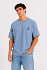 Remera de manga corta color celeste, de corte holgado y cuello redondo a la base, con un pequeño estampado de un ancla en el pecho.