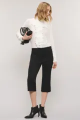 Pantalón capri negro de corte sastrero, confeccionado en tejido de punto grueso con elastano. Presenta calce slim, alforzas en el delantero, bolsillos ojal simulados, aberturas laterales en los bajos y cierre frontal con botón y broche metálico.