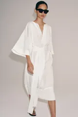 Vestido tipo túnica de corte evasé, color blanco, con escote en pico, mangas por debajo del codo y cinturón ajustable del mismo tejido.