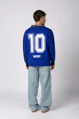 Camiseta de tejido de punto con cuello polo, manga larga y diseño inspirado en camisetas de fútbol retro. Presenta un color azul vibrante con un patrón geométrico lateral en negro y el número 10 estampado en el frente.