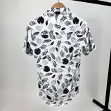 Camisa blanca con estampado de hojas en negro, de manga corta y cuello italiano.