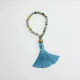 Handmala de meditación compuesto por 27 cuentas de piedra Amazonita de 8 mm, con un dije de Buda metálico, una cuenta de madera y una borla de hilo color turquesa.