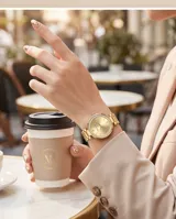 Reloj de pulsera analógico para mujer, con caja redonda de metal dorado y bisel decorado con cristales. Presenta una esfera minimalista en tono dorado con manecillas finas y una malla de eslabones metálicos a juego.