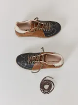 Championes de cuero con diseño tricolor en tonos negro, marrón y crema. Presentan cordones trenzados, costuras a la vista y detalle de pespuntes en el talón.