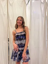Vestido corto de tirantes finos con estampado tie-dye en tonos azul, negro y gris. Presenta un escote recto con frunce central y un volado en el ruedo de una textura diferente.