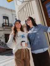 Remera de manga larga con diseño superpuesto que simula una camisa de rayas debajo. La prenda principal es de color azul piedra con estampado gráfico de Minnie Mouse y texto alusivo al tenis, mientras que las mangas y el cuello son de tela camisera a rayas celestes y blancas.