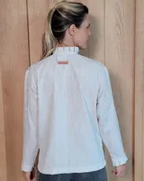 Camisa de manga larga con estampado de rayas verticales en tonos crudo y beige. Presenta cuello alto con volados, cierre frontal con botones dobles y puños con volados.