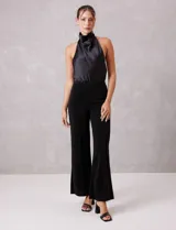 Pantalón wide leg de tiro alto confeccionado en tejido con acabado brillante tipo lurex. Presenta un corte recto y holgado con una costura vertical decorativa en el frente de cada pierna.