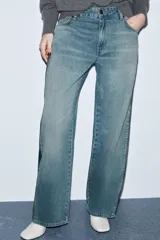 Jeans de tiro medio, corte recto y ancho, en denim azul claro con efecto lavado y desgaste. Presenta cierres metálicos completos a lo largo de las costuras laterales exteriores de ambas piernas.