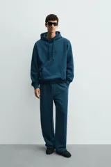 Sudadera con capucha de corte relajado, confeccionada en tejido de algodón con interior perchado. Presenta mangas largas, bolsillo frontal tipo canguro y terminaciones en rib.