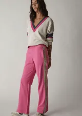 Sweater de punto color crema, con escote en pico con ribete rosa y gris. Presenta mangas largas con franjas grises y rosas en los puños, y logo bordado en el brazo.