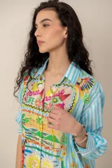 Camisa de manga larga con estampado tropical, fondo a rayas celestes y blancas, cuello camisero y cierre frontal de botones.