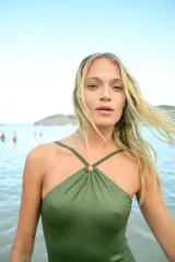 Malla enteriza color verde militar, confeccionada en lycra engomada. Presenta un diseño con cuello halter y un avío metálico circular en el centro del pecho, desde donde nacen las tiras ajustables. Posee corte de bombacha vedetina.