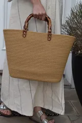 Bolso tipo shopper color marrón con textura trenzada, asas de mano rígidas símil bambú y detalles de tiras de cuerina marrón con tachas metálicas doradas.