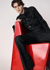 Chaqueta de denim en color negro, de corte clásico con cierre frontal de botones metálicos, cuello camisero y bolsillos con solapa en el pecho.