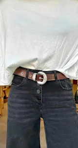 Cinto de cuero negro con textura gamuzada, presenta una hebilla metálica plateada de diseño redondeado con detalles grabados y pasador metálico a juego.