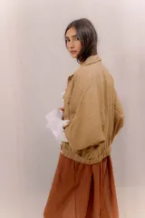 Campera liviana de lino color tostado, con cierre frontal de botones, bolsillos ojal en el pecho y mangas anchas con presilla y botón en los puños.