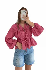 Blusa de manga larga amplia y abullonada, color fucsia, con frunces en el cuerpo y cordones ajustables con lazo en el escote y la cintura.