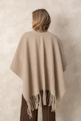 Ruana abierta de color beige, confeccionada en tejido de punto con terminación de flecos en el ruedo.