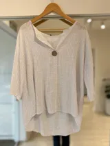 Blusa blanca de manga tres cuartos, escote en V con detalle de botón grande de madera y diseño asimétrico más largo en la parte trasera.