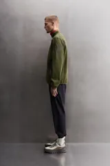 Chaqueta verde militar de punto con interior de polar. Tiene cuello alto, manga larga con bolsillo con cierre en la manga, bolsillos laterales con cierre y cierre frontal con cremallera.