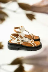 Sandalias negras de estilo chunky con plataforma dentada. Presentan tiras ajustables con cierre de velcro y hebillas metálicas, combinando texturas de cuero granulado y detalles en charol.