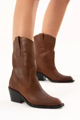 Bota de caña media con diseño estilo western, confeccionada en cuero con acabado texturado craquelado. Presenta tiradores laterales, puntera redondeada y taco cuadrado de altura media.