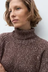 Polerón de cuello alto confeccionado en tejido buclé con textura jaspeada, de corte holgado y mangas largas con diseño raglán.