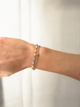 Pulsera doble de acero quirúrgico, compuesta por una cadena fina plateada y una cadena con pequeñas cuentas de colores pastel y esferas doradas.