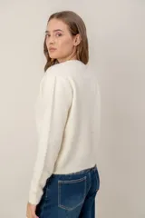 Cardigan de punto color crema con cuello redondo, manga larga y cierre frontal con botones forrados de distintos colores.