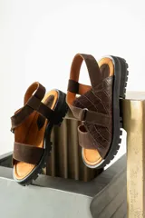 Sandalias de plataforma con suela track, confeccionadas en una combinación de cuero liso y cuero con textura croco. Presentan tiras anchas en el empeine y cierre con hebilla ajustable en el talón.