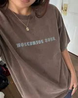 Remera marrón oversize con diseño gráfico estampado en la espalda que incluye la inscripción "Kaboa" y fechas de gira mundial.