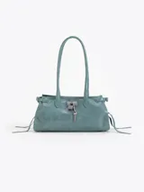 Cartera de hombro confeccionada en cuero vacuno color azul petróleo con acabado brillante. Presenta un diseño rectangular con herraje metálico tipo candado y dijes colgantes en el frente, además de correas laterales ajustables con tiras decorativas.