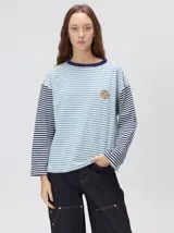 Remera de manga larga con diseño a rayas horizontales en tonos celestes y blancos en el cuerpo, y mangas a rayas azul marino y blancas. Presenta cuello redondo en color azul marino, logo bordado en el pecho y calce holgado.