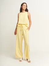 Pantalón de lino color amarillo pastel, de tiro alto y corte palazzo, con elástico en la cintura, bolsillos laterales y dobladillo invisible.