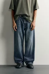 Jeans de denim de algodón en color azul con efecto desgastado, tiro medio y corte recto de ajuste holgado (loose fit). Cuenta con diseño clásico de cinco bolsillos y cierre frontal con cremallera y botón.
